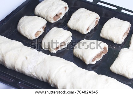 Preparation of cinnamon rolls. The woman sends to the oven billets of rolls and rolls with cinnamon, laid on a baking tray.
