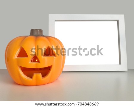 Happy Halloween background. Pumpkin toy smiling face. Plastic Jack o lantern with light. Horizontal white photo frame mock up template on the table. Empty space. Trick or treat. Holiday sign symbol.