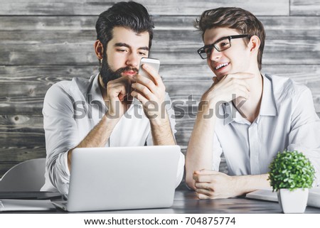 Two handsome businessmen using cellular phone at hipster office workplace. Wooden wall background. Technology, modern social media, leisure concept 