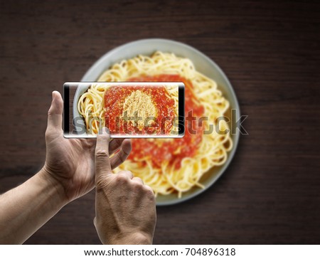 Two hands holding a mobile Smartphone and take a picture a Dish of spaghetti bolognese on wooden texture