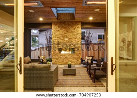 Dreamy outdoor covered patio with stone fireplace, a beadboard ceiling with skylight, rattan armchairs, sofa and ottomans overlooking the expansive backyard. Northwest,USA
