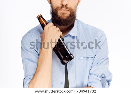 A glass bottle in the hand of a man with a beard on a light background                               