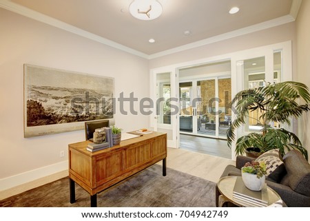 Light and airy office features a wooden desk placed in the center of the room on a grey rug in front of a grey armchair and decorative green plant in a pot. Northwest, USA
