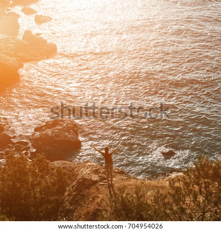 Back view of woman standing on the sea coast Between pines and Enjoying the sunset