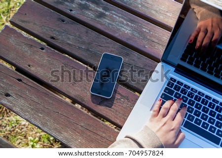 Young Woman working on laptop outdoors with her phone on her side.
