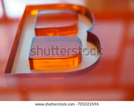 Big "B" letter shape groove engraved on red orange thick transparent acrylic glass, perspective shot with sunlight reflection from window