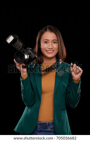 Portrait of happy Asian woman with digital camera in one hand and glasses in another