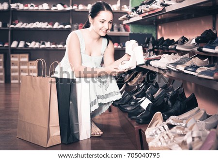 Smiling russian  girl is choosing heeled sandals in shoes shop.