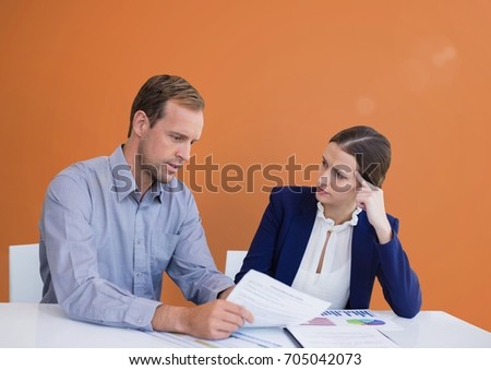 Digital composite of Business people at a desk looking at a paper against orange background