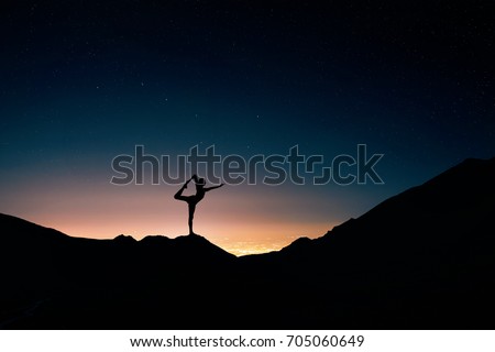 Fit Man in silhouette doing yoga natarajasana pose at night city and starry sky background