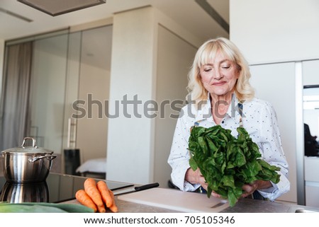 Picture of cheerful mature woman at home cooking in kitchen. Looking aside.