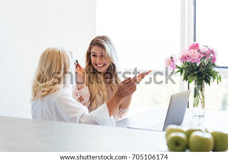 Picture of smiling young lady sitting at home with her grandmother using laptop computer. Looking aside.