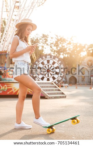 Image of concentrated young woman with skateboard outdoors. Looking aside.