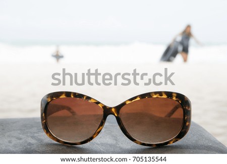 Sunglasses putting on rock table with people playing on the beach.