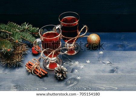 hot drink of mulled wine or tea with cinnamon spice stick in glass near christmas decorative ball, fir tree and pinecone on grey wooden background, copy space