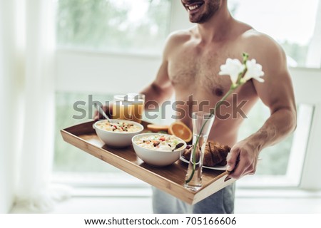 Good morning! Cropped image of handsome sporty man is standing with healthy breakfast in hands.