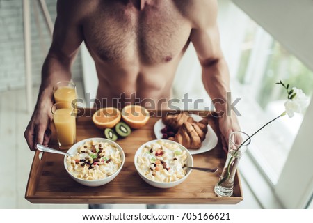 Good morning! Cropped image of handsome sporty man is standing with healthy breakfast in hands.