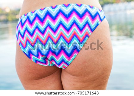 Close up picture of a caucasian young woman's back & butt having cellulite, posing in colorful swimwear