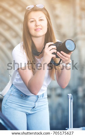 Portrait of blond smiling girl holding camera in hands and photographing in city