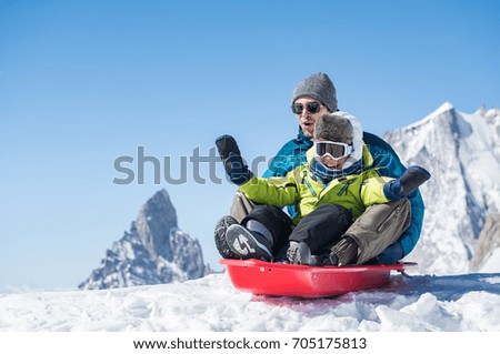 Father and son sledding during winter holiday. Happy dad and little boy playing with snow sled. Man with smiling child sitting on bobsledge in the snow with copy space.
