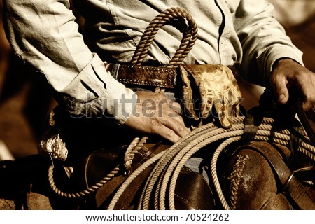 Close up of the hands and torso of an authentic working cowboy in the American West riding to work in sunset light (sepia/brown tint).