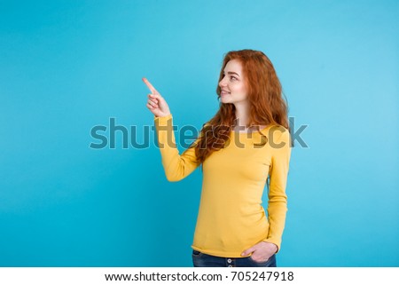 Close up Portrait young beautiful attractive redhair girl happy with something and pointing finger. Blue Pastel Background. Copy space.