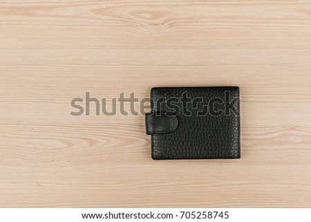 Black leather purse lying on a wooden table. View from above