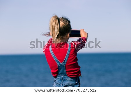 girl taking picture with phone outside. kid holding smartphone on northern europe sea side. small preschooler child using mobile phone outdoors.