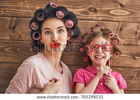 Funny family! Mother and her child daughter with a paper accessories. Cute girl holding lips on stick. Beautiful young woman holding glasses.