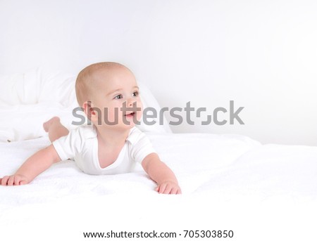 Infant child baby boy lying happy smiling on white blanket. Cute newborn on white light background