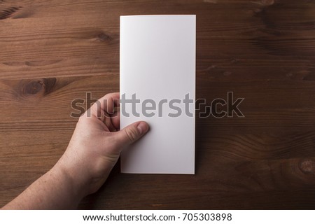 Blank tri fold brochure in hand on wooden background to replace your design or message. A mock-up for brand identification for designers 