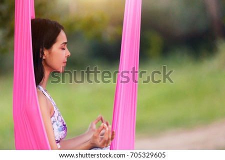 Portrait of beautiful smiling young woman enjoying aerial yoga, relaxing, breathing fresh air, calm and dreaming concept, in green park, copy space