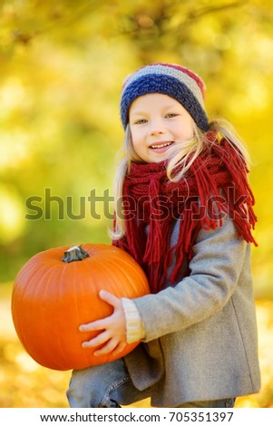 Adorable little girl having fun on a pumpkin patch on beautiful autumn day outdoors. Happy child playing in autumn park. Kid gathering yellow fall foliage. Autumn activities for children.