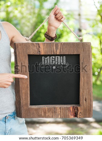 Restaurant menu on wooden board hold by woman hand outdoor. Template mock up