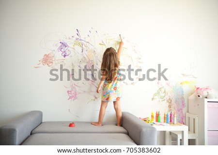 Curly cute little toddler girl painting with paints color and brush on the wall. Works of child Royalty-Free Stock Photo #705383602
