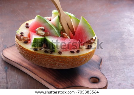Melon stuffed with watermelon, sprinkled with walnut on a wooden board