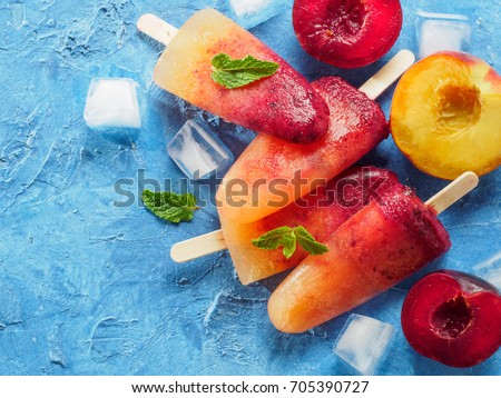 Close up view of plum and peach popsicle on blue concrete background. Fruit and red sangria, lemonade or mojito popsicles ice cream. .With fresh plums and peach. Copy space.
