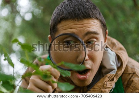 Photo of young botanist with magnifying glass in forest on summer day