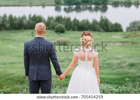 The bride and groom stand on the background of the river. Happy bride and groom stand holding hands.