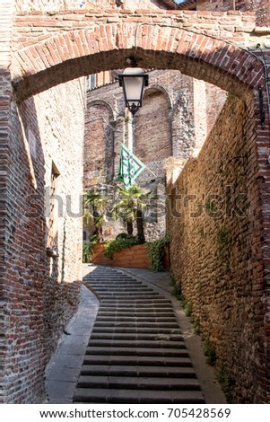 Brick arch with staircase and black and green flag in the center of an ancient Italian city