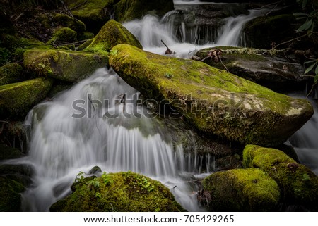 Close Up of Rushing Water Around Mossy Boulders in summer