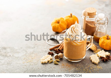 Pumpkin spice latte in a glass mug with cinnamon, nutmeg and cookies