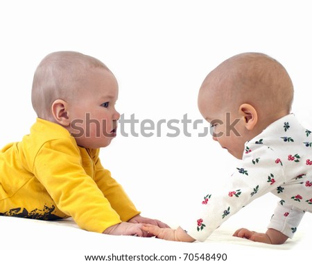 Two funny baby on a white mattress standing on all fours and look at each other