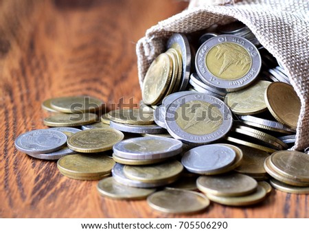 selective focus, yellow gold coins falling from potato brown sack  on wood table top background, money concept
