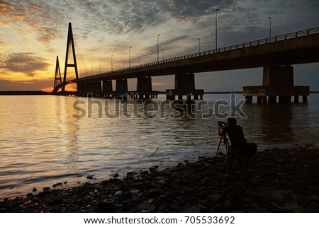 Photographer waiting to take a photo of beautiful sunset at  Senai-Desaru bridge of Sungai Johor. The long exposure image contain certain grain or noise and soft focus when view at full resolution. 