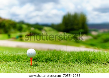 close up of white golf ball on orange tee on green grass with blue sky and cloud and view of mountain background in sunny day. copy space for your text.