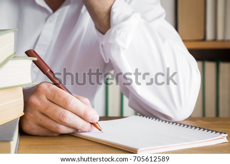 Man's hand with pen writing something in the notebook on the table. Education concept.