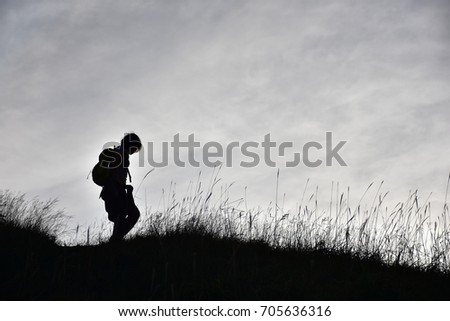 hiker woman with backpack walking on top of mountain  in sunset moment, silhouette gold background 