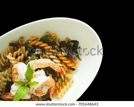 This is Thai - Italian fusion food dish. The picture of fusilli and shrimp with Thai basil in white dish on  black background.