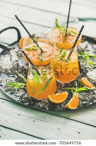 Refreshing cold alcoholic summer citrus cocktail with orange, peppermint and crushed ice in stemless glasses on dark tray over light wooden background, selective focus, copy space